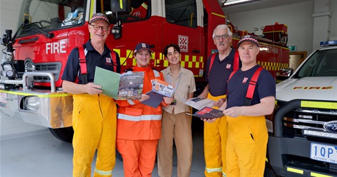 5 people standing and smiling at camera, 3 in fire fighter uniform and 1 in SES uniform and one council worker. They are holding various paper resources.